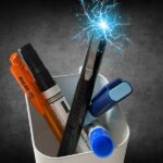 Pojemnik z długopisami i narzędziami, z których jeden emituje niebieskie wyładowania elektryczne.