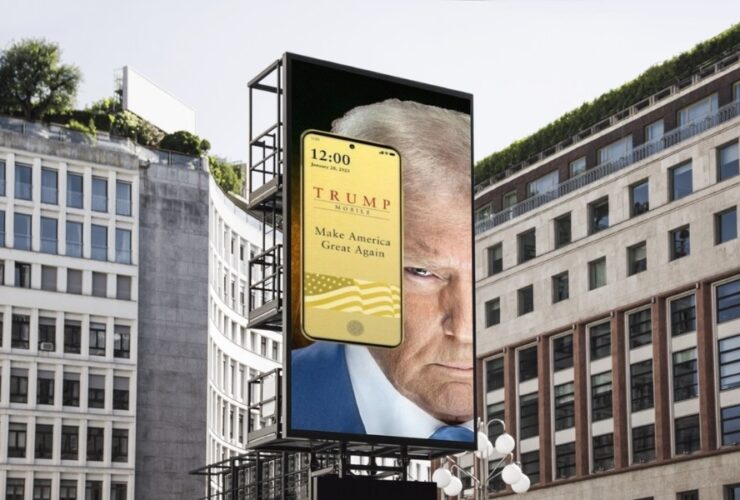 Bilboard z wizerunkiem Donalda Trumpa i smartfonem Donalda Trumpa T1 Mobile. W tle budynki biurowe.