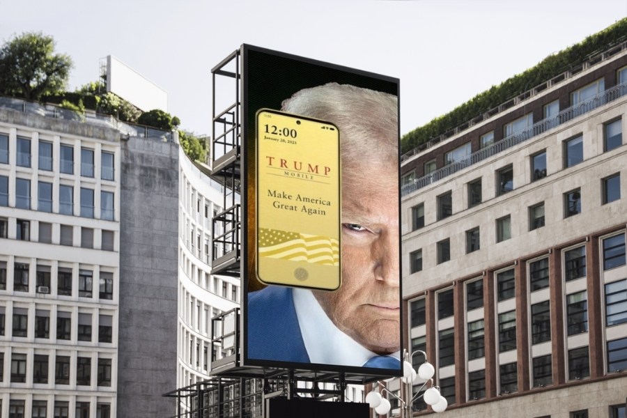 Bilboard z wizerunkiem Donalda Trumpa i smartfonem Donalda Trumpa T1 Mobile. W tle budynki biurowe.