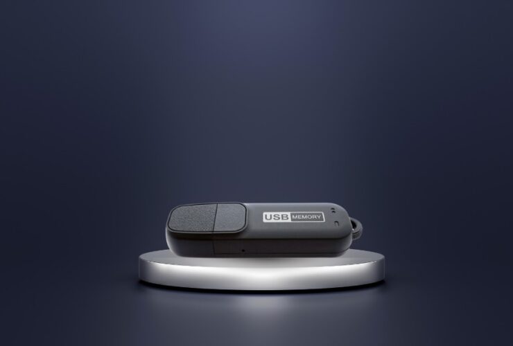Dyktafon ukryty w pendrive MQ-U310 na szarej podstawce. Tło w ciemnych barwach.