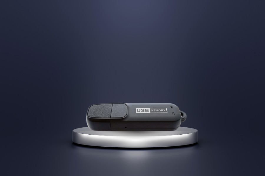 Dyktafon ukryty w pendrive MQ-U310 na szarej podstawce. Tło w ciemnych barwach.