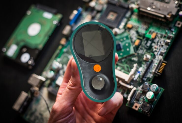 Lupa cyfrowa Inskam 370 w zielonej obudowie trzymana w dłoni. W tle układy scalone komputera.