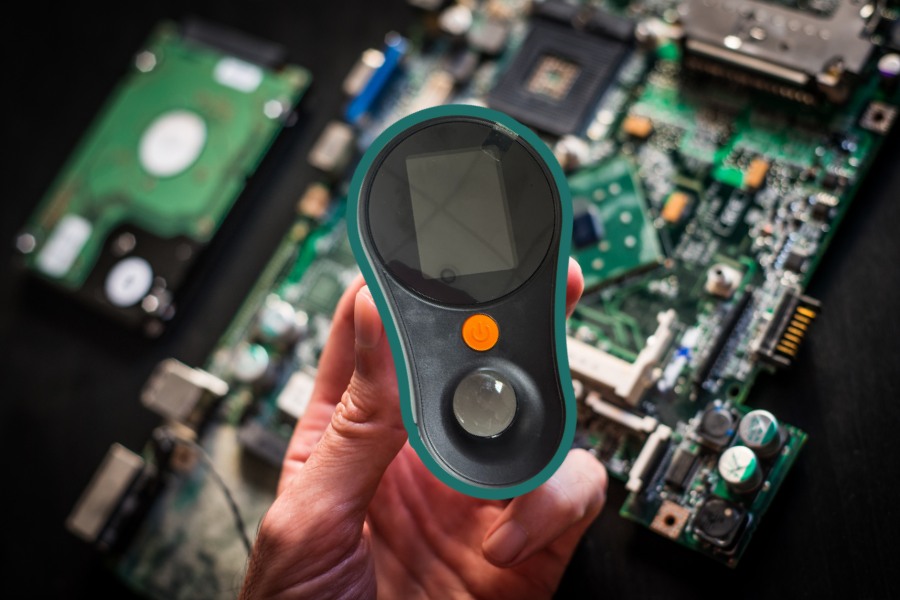 Lupa cyfrowa Inskam 370 w zielonej obudowie trzymana w dłoni. W tle układy scalone komputera.