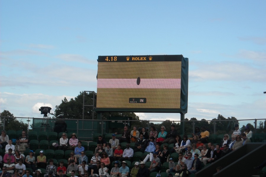 Wizualizacja śladu piłki zobrazowana przez system Hawk-Eye, widoczna na telebimie podczas meczu tenisowego. Na dole widoczni kibice na trybunach.