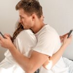 Mężczyzna i kobieta przytulają się na łóżku, każde z nich używa swojego telefonu. Pokazuje to, że tak naprawdę są oni sobie obojętni.