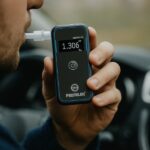 Mężczyzna wykonujący pomiar alkomatem Promiler iSober 50 w samochodzie – na wyświetlaczu widoczny wynik 1.306‰.