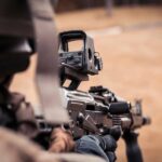 Żołnierz lub strzelec patrzący przez celownik kolimatorowy zamontowany na karabinie, widok zza ramienia.