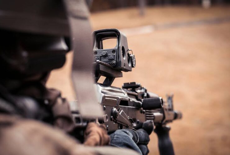 Żołnierz lub strzelec patrzący przez celownik kolimatorowy zamontowany na karabinie, widok zza ramienia.