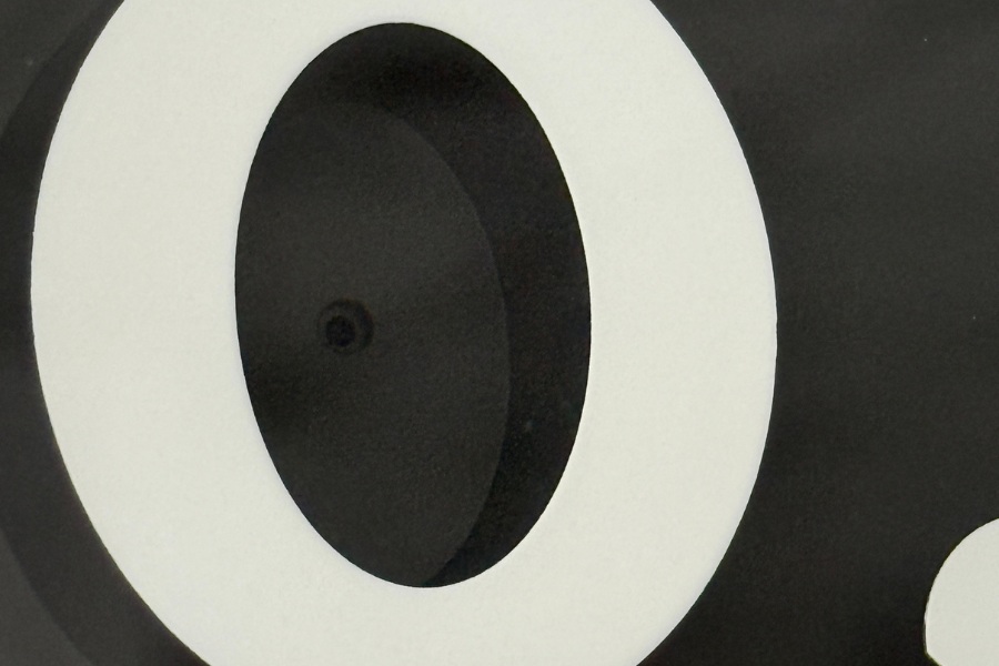 Zbliżenie na cyfrę "0" w liczbie 10, gdzie ukryty jest miniaturowy obiektyw. Widoczny jest jego zarys.