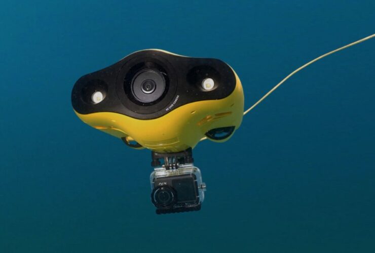 Na zdjęciu został przedstawiony żółty dron podwodny z kamerą zanurzony w wodzie, podłączony przewodem.