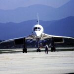 Fotografia przedstawiająca samolot naddźwiękowy kołujący na pasie startowym. W tle widoczny zarys wysokich gór.