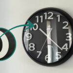 Ukryta kamera w zegarze ściennym DVR-259. W mniejszej ilustracji zbliżenie na ukryty obiektyw i strzałka wskazująca na miejsce jego montażu.