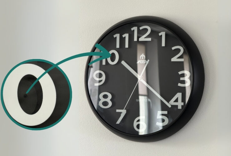 Ukryta kamera w zegarze ściennym DVR-259. W mniejszej ilustracji zbliżenie na ukryty obiektyw i strzałka wskazująca na miejsce jego montażu.