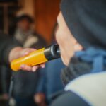 Kobieta podczas policyjnej kontroli dmucha w alkomat, aby sprawdzić poziom alkoholu w wydychanym powietrzu.