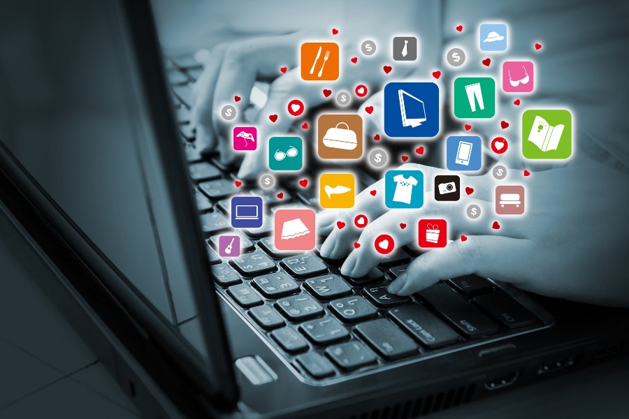 Ręce na klawiaturze laptopa, z którego ekranu wyskakują kolorowe ikony powiadomień symbolizujące nadmiar informacji w sieci.