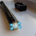 Najmocniejszy paralizator na rynku bez zezwolenia Paralyseur X8 leży na białym blacie. W tle widoczna ładowarka akumulatorów. W górnej części urządzenia widać błysk prądu.