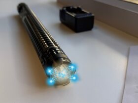 Najmocniejszy paralizator na rynku bez zezwolenia Paralyseur X8 leży na białym blacie. W tle widoczna ładowarka akumulatorów. W górnej części urządzenia widać błysk prądu.