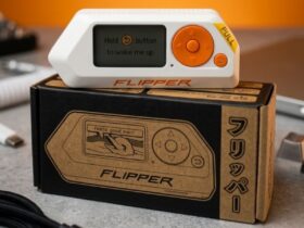 Urządzenie Flipper Zero z pomarańczowymi przyciskami leży na pudełku.