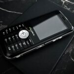 Telefon Tripleton Enigma E2 leży na czarnym pudełku na marmurowym blacie.