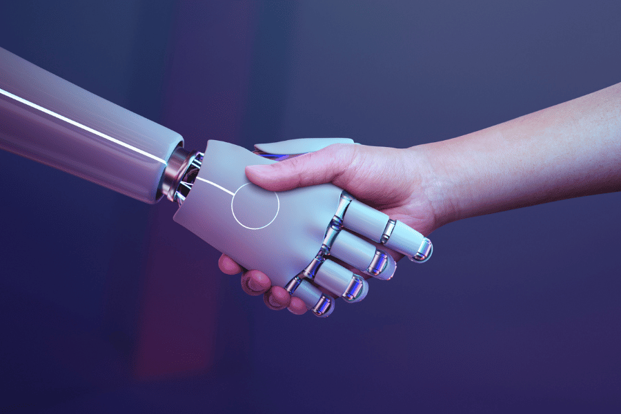 Ludzka dłoń ściska dłoń humanoidalnego robota na ciemnym, fioletowo-niebieskim tle.